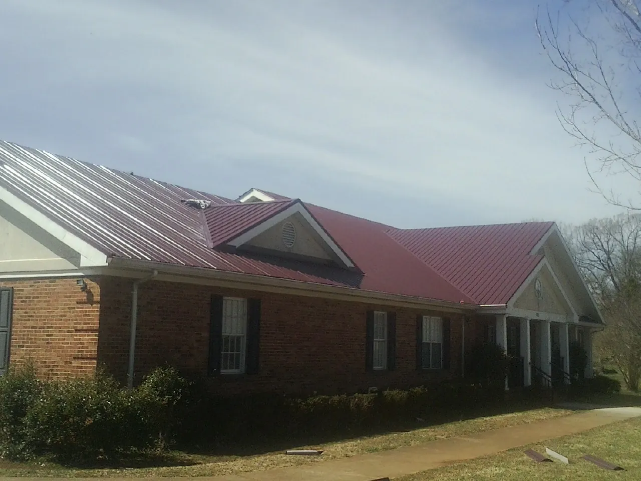 Red metal roof with gabled entries on a long brick building, from a Hail Damage Roof Repair job in La Conner