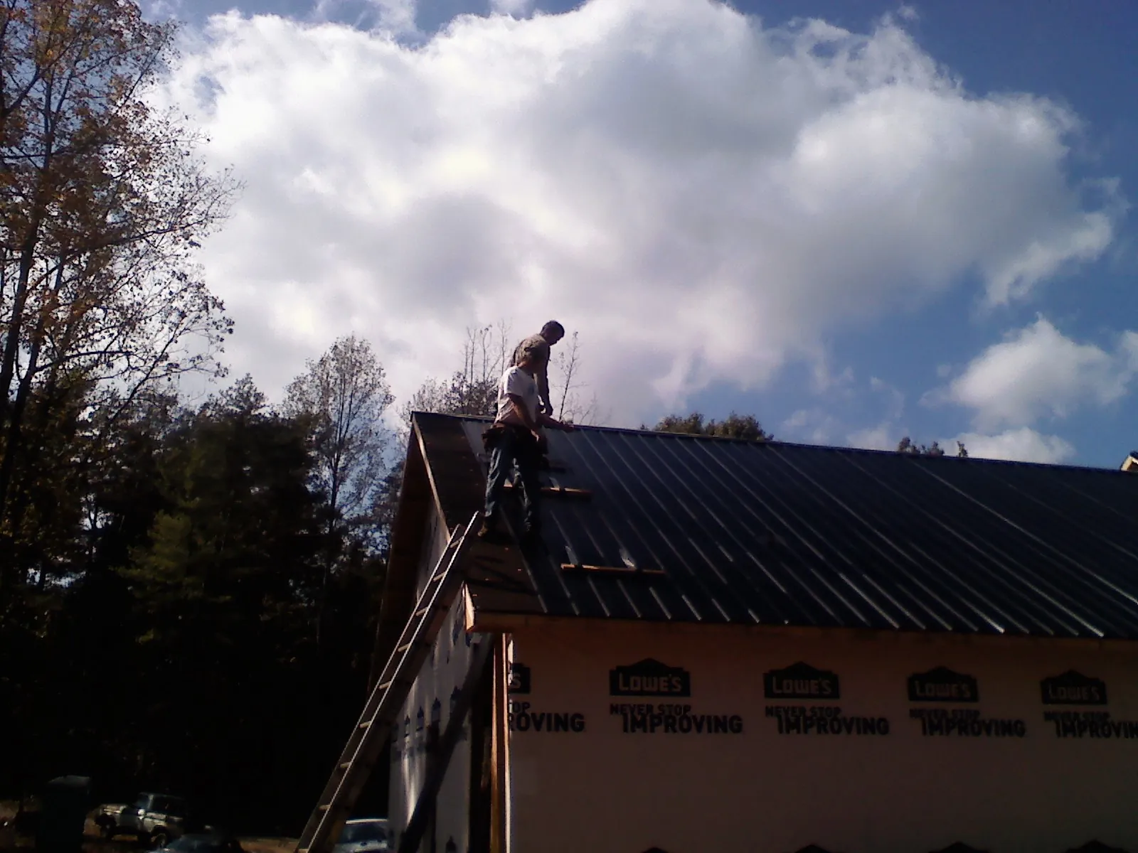 Roofer fastening dark metal panels high against a cloudy sky, from a Roof Inspection job in La Conner