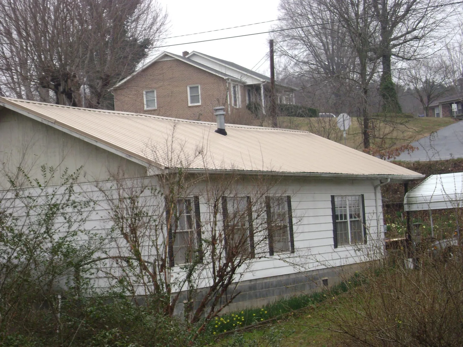 Tan metal roof on a white sided house set into a hillside — Commercial Roofing by Roofing Brothers in La Conner